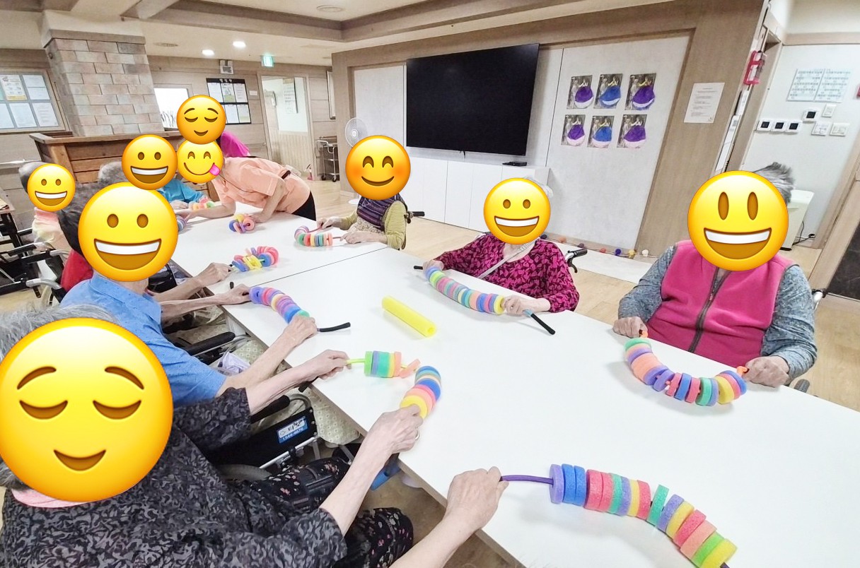 어르신들이 테이블에 둘러앉아 알록달록한 스펀지 링을 끈에 꿰는 소근육 활동을 하는 모습