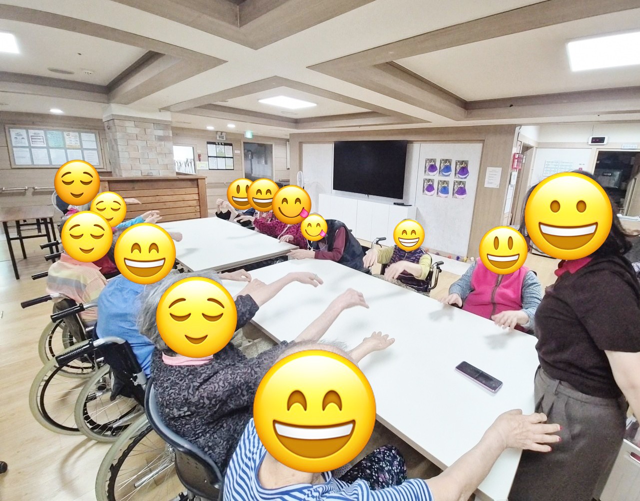 어르신들이 테이블에 둘러앉아 두 팔을 앞으로 뻗으며 체조를 따라 하는 모습