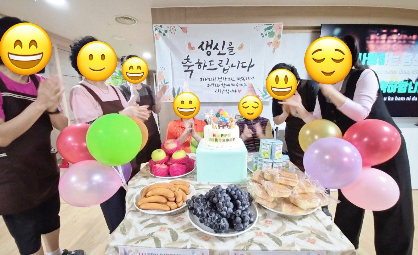 케이크와 과일, 풍선으로 차린 생신상 앞에서 직원들이 박수로 어르신의 생신을 축하하는 모습